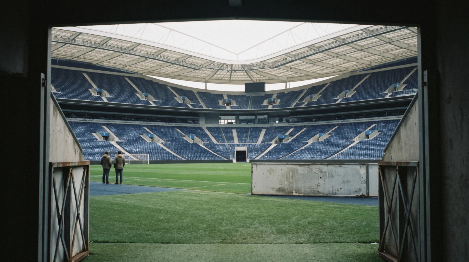 The blue seats and open bowl of the Estadio do Dragao seen from the tunnel mouth at pitch level at 11:15 on a weekday, two visitors small and seen from behind on the touchline, fc porto museum