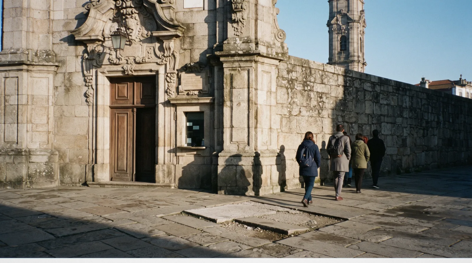 The ticket window beside the granite doorway of the Torre dos Clérigos on a bright morning with a short queue, where Porto attractions tickets are sold