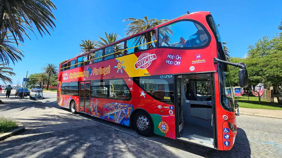 A red City Sightseeing hop-on hop-off bus parked under palms in Porto