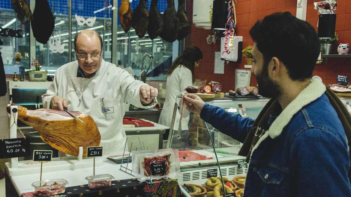 A butcher slicing cured ham for a customer at a Porto market counter