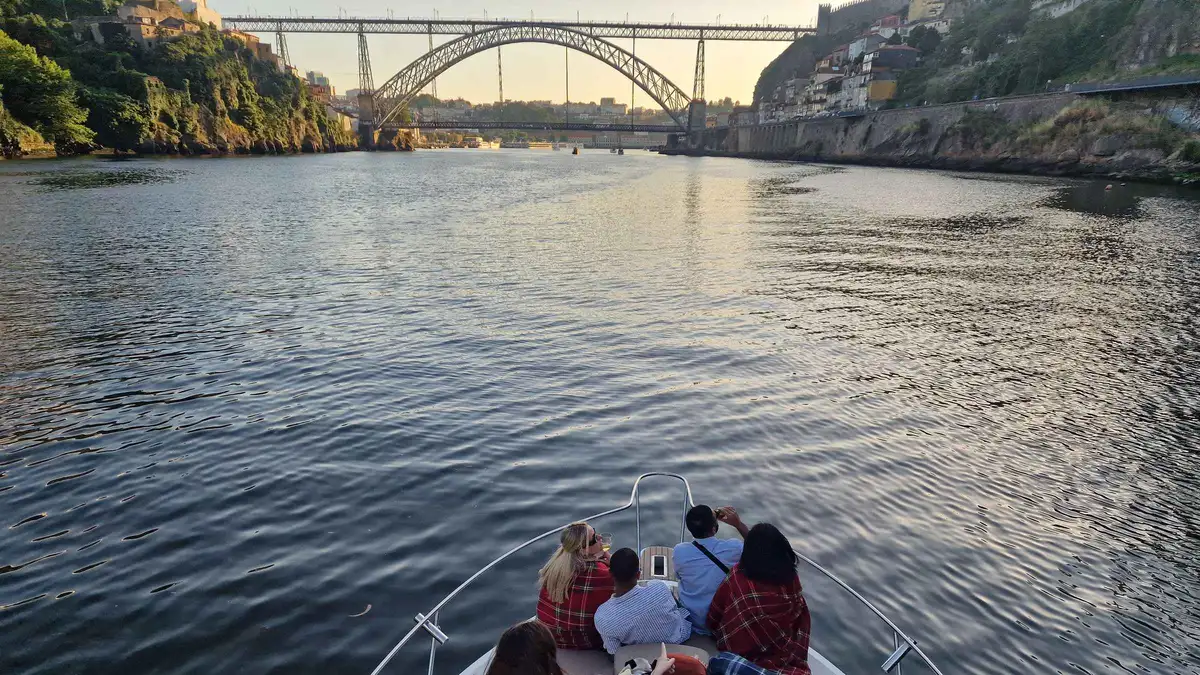 Passengers on a small boat approaching the arched Maria Pia bridge on the Douro in Porto