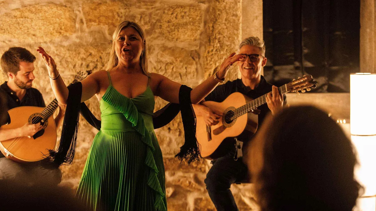 A fado singer in a green dress performing with guitarists in a stone-vaulted room in Porto