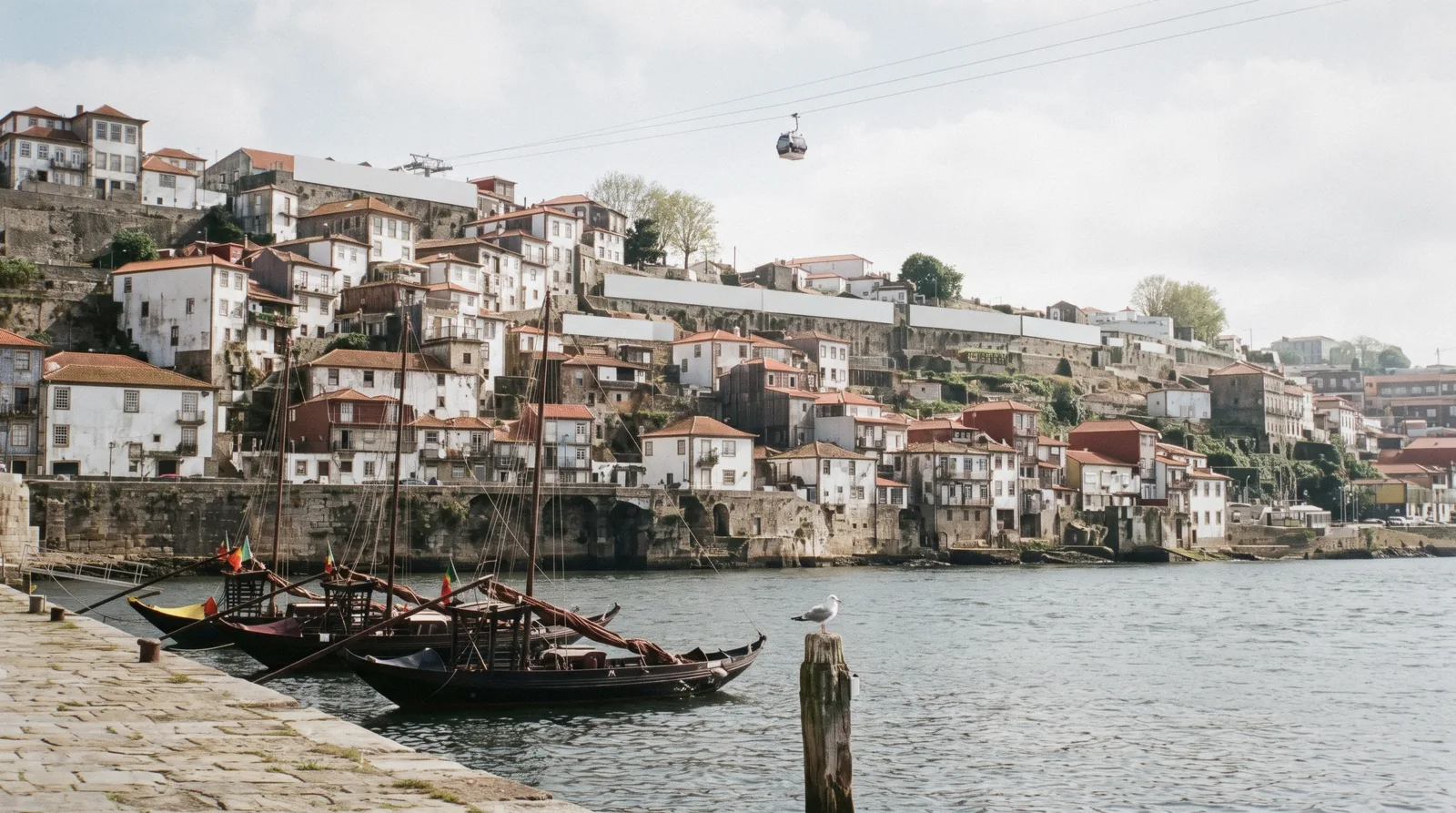 The lodge roofs and rabelo boats of the Cais de Gaia at 18:15 with the iron arch of the Luis I bridge and the Porto bank behind, Vila Nova de Gaia